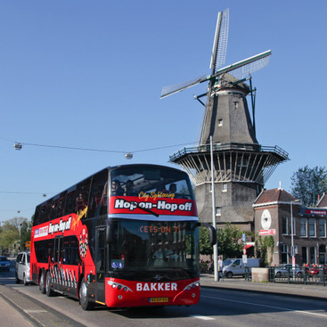 A double decker bus moving on a road. On it, a small antennae like device.